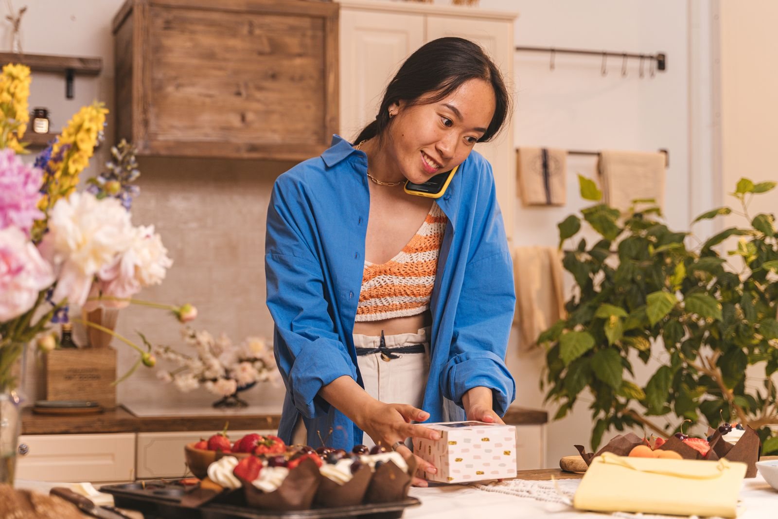 A bakery owner on a phone call while boxing an order of cupcakes at her counter