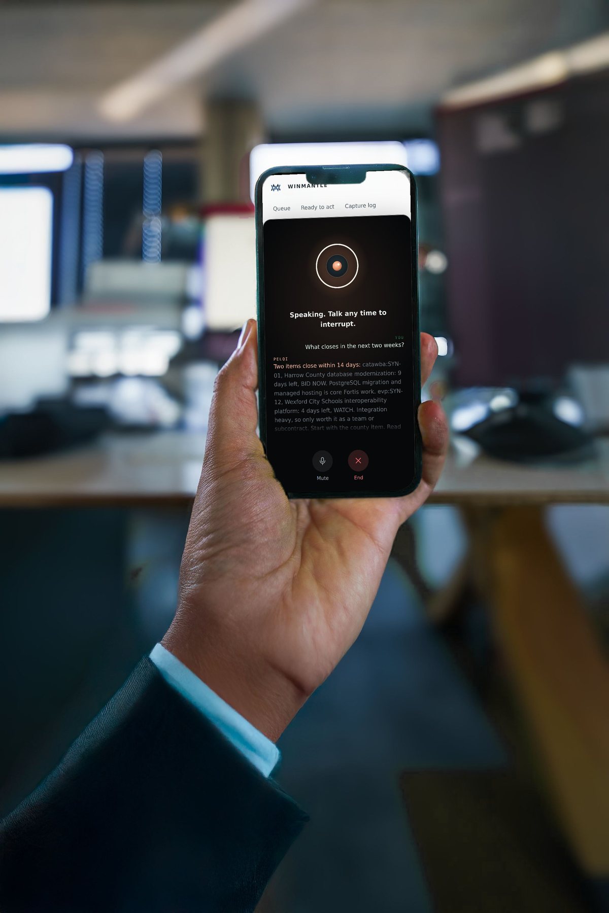 A hand holding an iPhone in an office, showing a voice conversation with PelQi in Winmantle: the question, and PelQi reading out what closes in the next two weeks